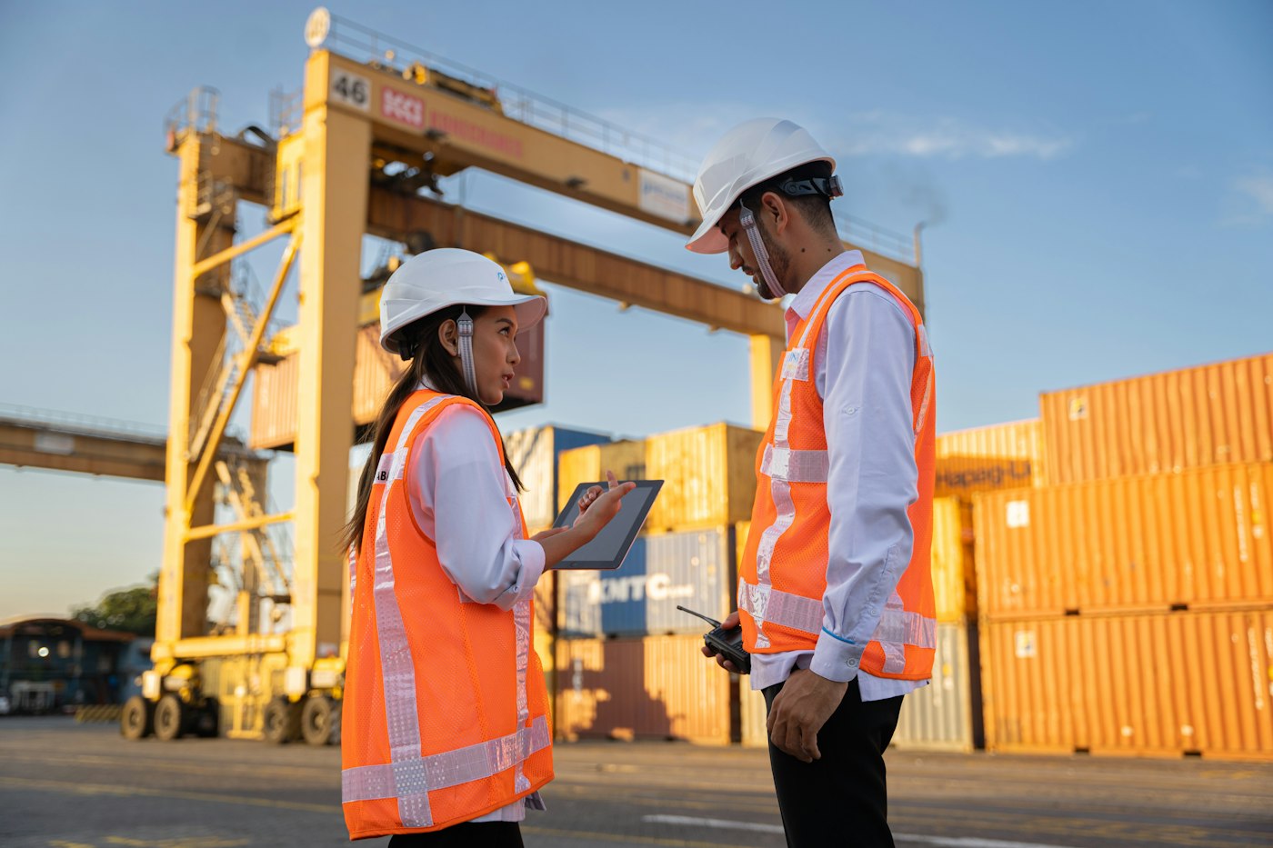 Two engineers in hard hats reviewing a tablet on site